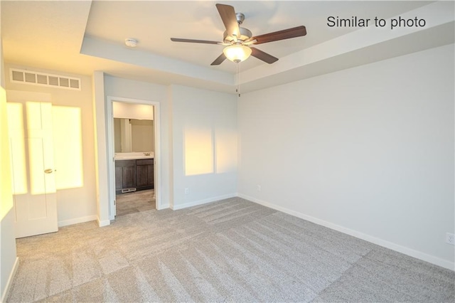 unfurnished bedroom with a raised ceiling, connected bathroom, light colored carpet, and ceiling fan