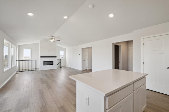 kitchen featuring a center island, a fireplace, light countertops, light wood-style floors, and vaulted ceiling