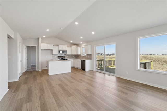 kitchen with lofted ceiling, open floor plan, appliances with stainless steel finishes, light wood-type flooring, and backsplash