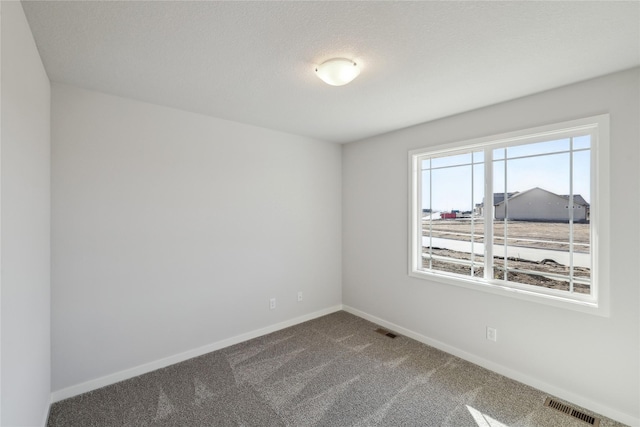 unfurnished room featuring a textured ceiling, dark carpet, visible vents, and baseboards