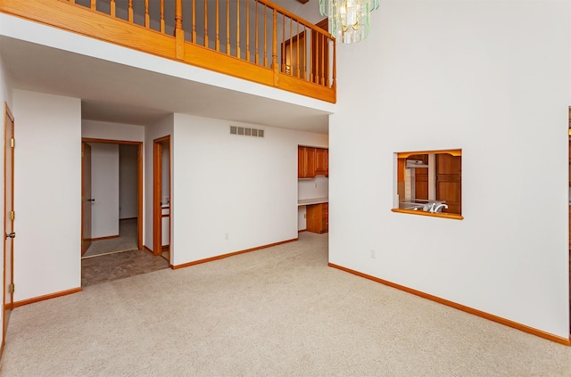 unfurnished living room featuring a notable chandelier, light carpet, and a high ceiling