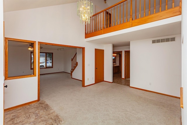 unfurnished living room featuring light carpet, ceiling fan with notable chandelier, and a high ceiling