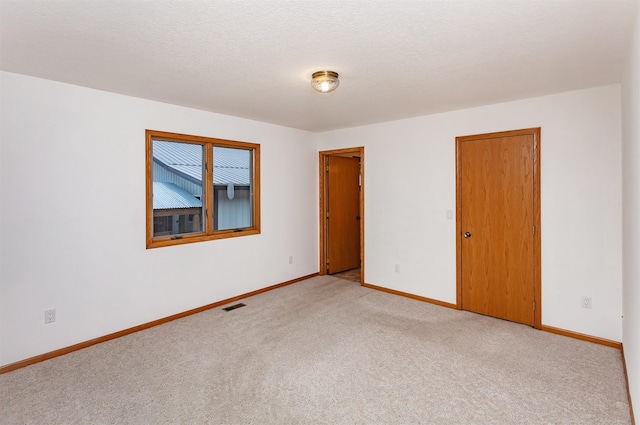 unfurnished room featuring baseboards, visible vents, a textured ceiling, and light colored carpet