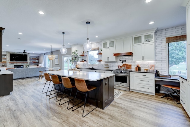 kitchen featuring white cabinets, a kitchen breakfast bar, high end range, hanging light fixtures, and light hardwood / wood-style flooring