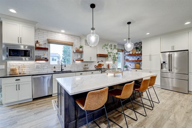 kitchen featuring a kitchen island, appliances with stainless steel finishes, white cabinetry, sink, and dark stone countertops