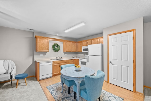 kitchen with white appliances, light countertops, a sink, and light wood finished floors