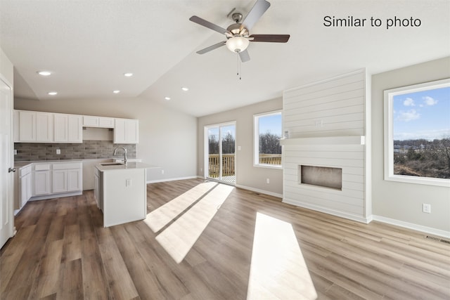 kitchen featuring lofted ceiling, a kitchen island with sink, white cabinets, decorative backsplash, and wood-type flooring