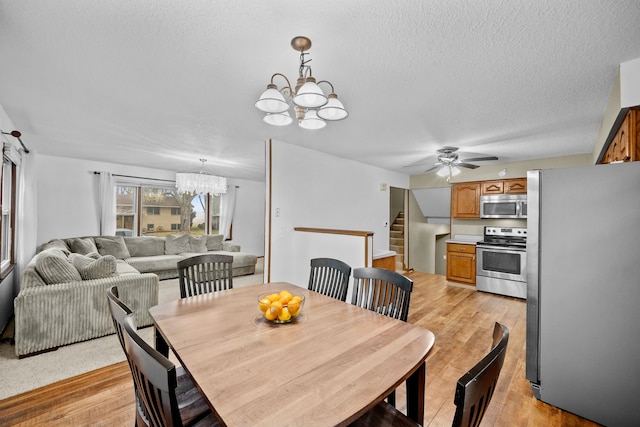 dining room with ceiling fan with notable chandelier, light hardwood / wood-style floors, and a textured ceiling