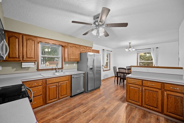 kitchen with hardwood / wood-style floors, ceiling fan with notable chandelier, hanging light fixtures, sink, and appliances with stainless steel finishes