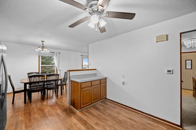 dining area with a textured ceiling, light hardwood / wood-style floors, and ceiling fan with notable chandelier