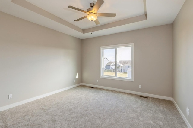 unfurnished room with ceiling fan, a raised ceiling, and light colored carpet