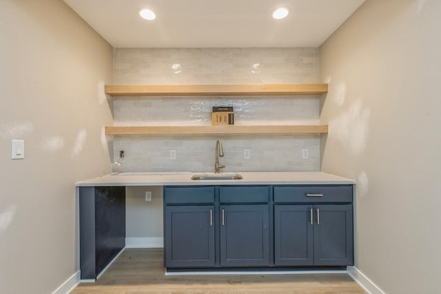 bar featuring blue cabinetry, light hardwood / wood-style flooring, sink, and tasteful backsplash