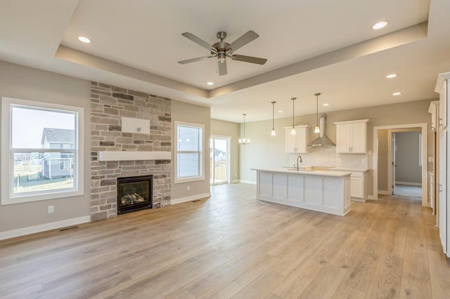 unfurnished living room with sink, ceiling fan, light wood-type flooring, a fireplace, and a tray ceiling