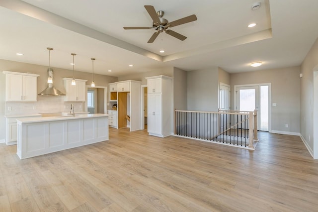 kitchen featuring white cabinetry, wall chimney exhaust hood, light hardwood / wood-style flooring, an island with sink, and pendant lighting