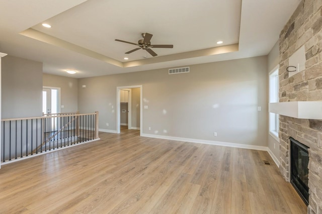 unfurnished living room featuring ceiling fan, light hardwood / wood-style floors, a fireplace, and a tray ceiling