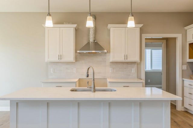 kitchen with a kitchen island with sink, white cabinets, sink, light stone countertops, and decorative light fixtures