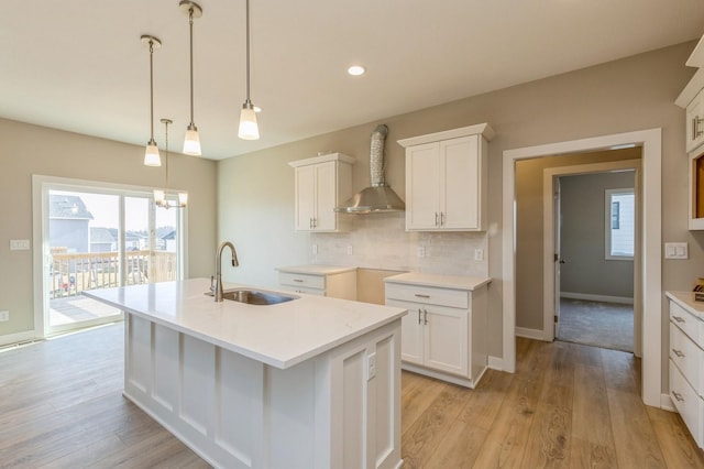 kitchen with a center island with sink, white cabinetry, wall chimney exhaust hood, and sink