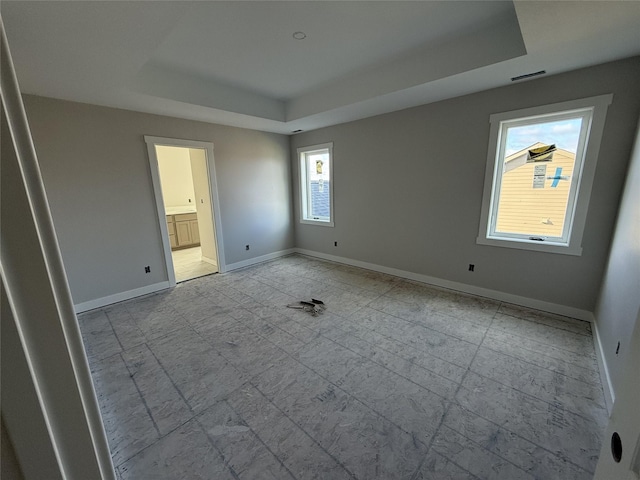 unfurnished bedroom featuring a raised ceiling and ensuite bath