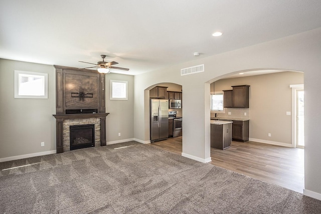 unfurnished living room with a stone fireplace, carpet floors, and a healthy amount of sunlight