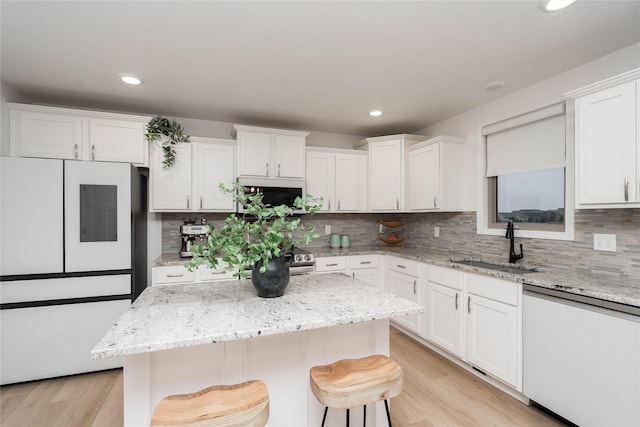 kitchen with light stone countertops, white appliances, sink, a center island, and a breakfast bar area