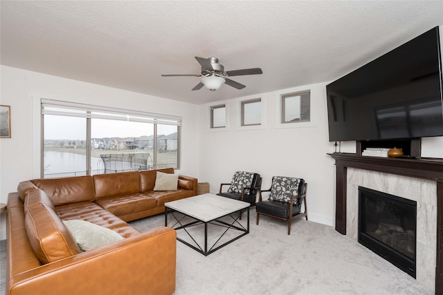 living room with a water view, a ceiling fan, a textured ceiling, carpet, and a tile fireplace