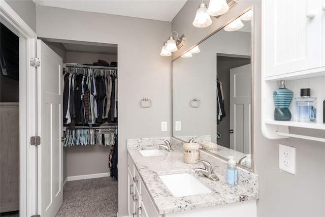 bathroom featuring a sink, baseboards, double vanity, and a spacious closet