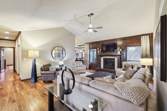 living room featuring a textured ceiling, ceiling fan, light hardwood / wood-style flooring, and vaulted ceiling