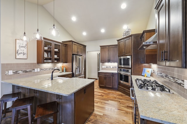 kitchen featuring kitchen peninsula, appliances with stainless steel finishes, light stone counters, vaulted ceiling, and hanging light fixtures