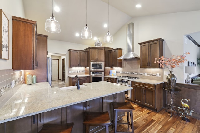 kitchen with pendant lighting, backsplash, wall chimney range hood, vaulted ceiling, and stainless steel appliances