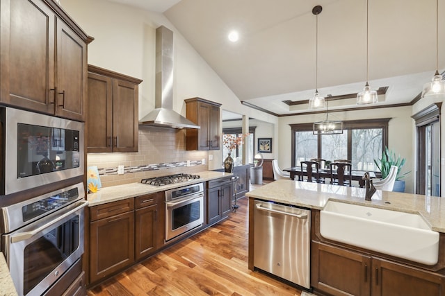 kitchen with light stone counters, hanging light fixtures, stainless steel appliances, and wall chimney range hood