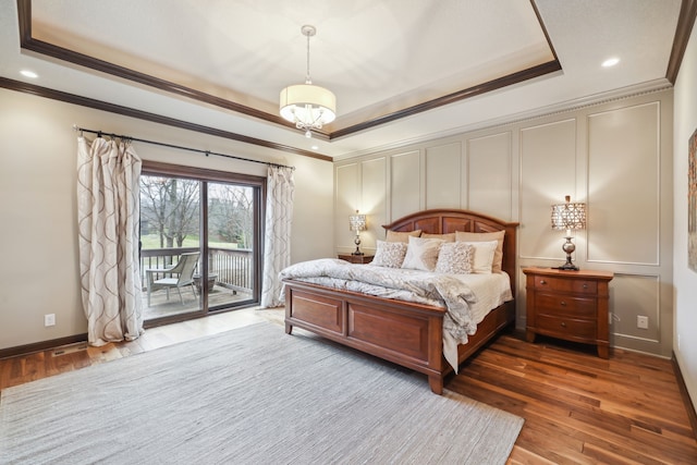 bedroom with access to exterior, wood-type flooring, a tray ceiling, and ornamental molding