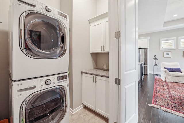 clothes washing area featuring stacked washing maching and dryer, cabinet space, light wood-style flooring, and baseboards