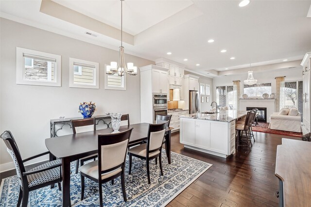 dining area with dark hardwood / wood-style floors, an inviting chandelier, sink, and a tray ceiling