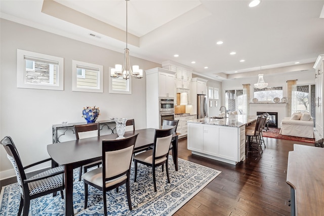 dining room with dark wood-type flooring, a fireplace, visible vents, a raised ceiling, and an inviting chandelier