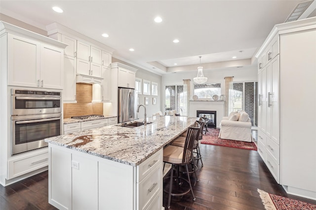 kitchen with a spacious island, a sink, white cabinets, open floor plan, and appliances with stainless steel finishes