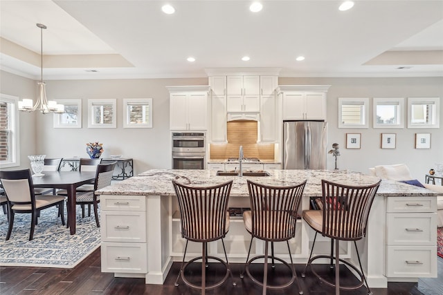 kitchen featuring white cabinets, a center island with sink, light stone counters, and stainless steel appliances