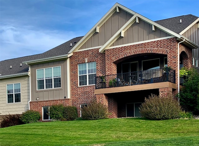 rear view of property featuring a yard, a shingled roof, board and batten siding, and brick siding