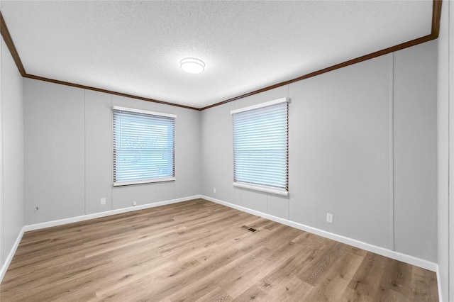 spare room with light wood-type flooring, ornamental molding, and a textured ceiling