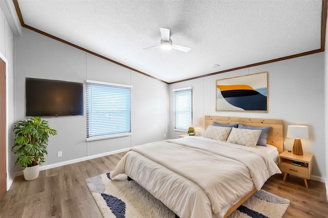 bedroom with a textured ceiling, hardwood / wood-style flooring, vaulted ceiling, ceiling fan, and crown molding