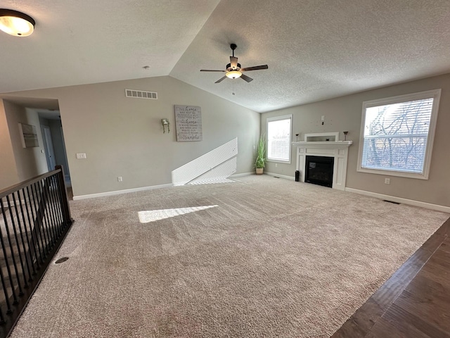 unfurnished living room with dark carpet, a textured ceiling, vaulted ceiling, and ceiling fan