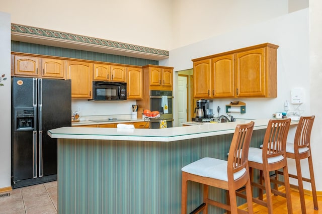 kitchen featuring black appliances, a breakfast bar, kitchen peninsula, and light tile patterned floors