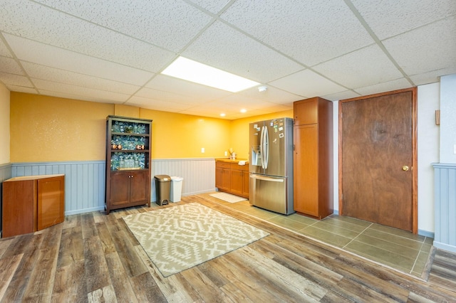 interior space with stainless steel fridge, a drop ceiling, and hardwood / wood-style floors