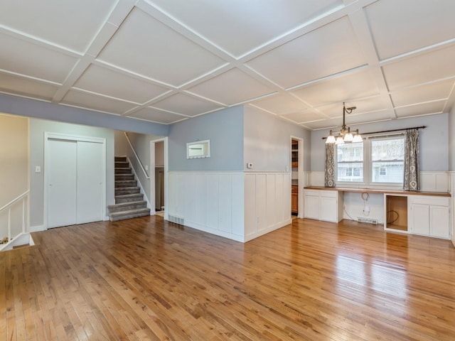 unfurnished living room with light hardwood / wood-style flooring, coffered ceiling, and an inviting chandelier