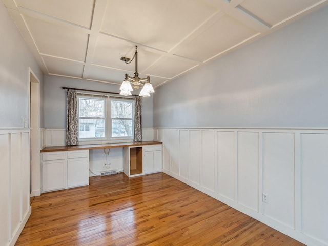 unfurnished office with a notable chandelier, light hardwood / wood-style floors, built in desk, and coffered ceiling