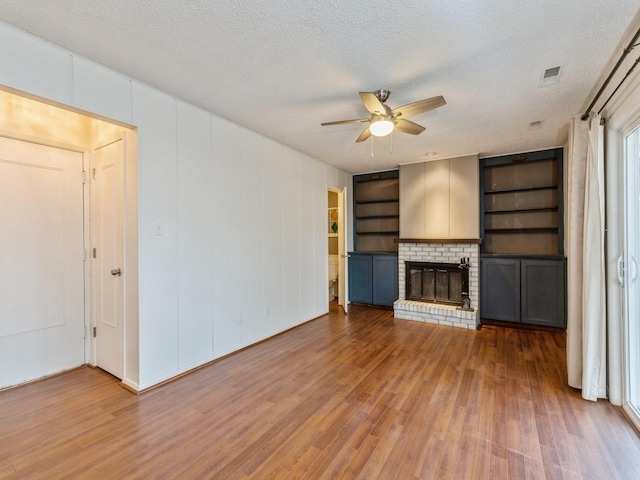 unfurnished living room with ceiling fan, built in features, wood-type flooring, a textured ceiling, and a fireplace