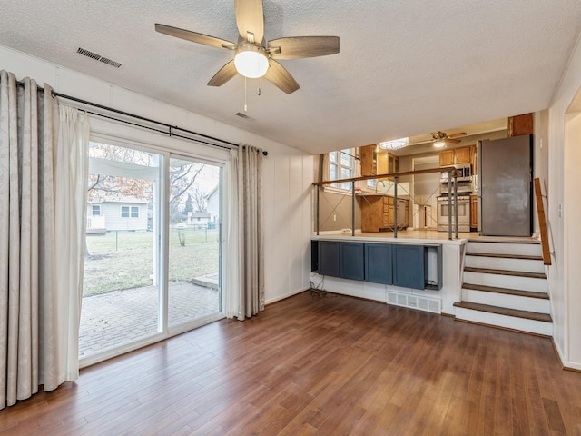 unfurnished living room with a textured ceiling, ceiling fan, and dark wood-type flooring