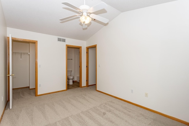 unfurnished bedroom with a walk in closet, vaulted ceiling, ceiling fan, a closet, and light colored carpet