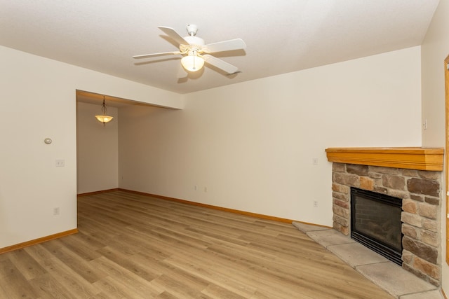 unfurnished living room featuring ceiling fan, a stone fireplace, and light wood-type flooring