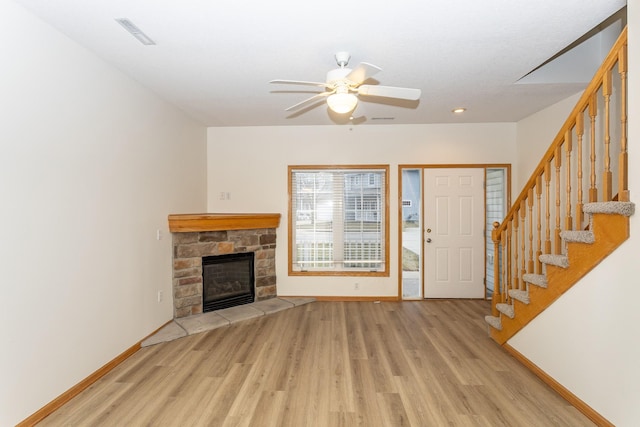 unfurnished living room with a stone fireplace, ceiling fan, and light wood-type flooring