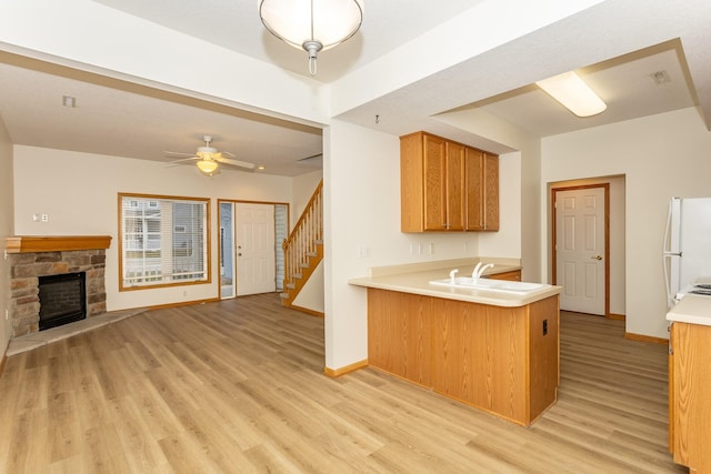 kitchen featuring sink, white refrigerator, kitchen peninsula, a fireplace, and light hardwood / wood-style floors